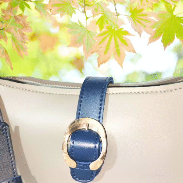 Elegant beige and navy moon-shaped handbag with gold buckle and shoulder strap
