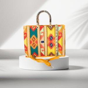 Colorful tribal pattern handbag with yellow tones, acrylic handle, and shoulder strap displayed on a white platform