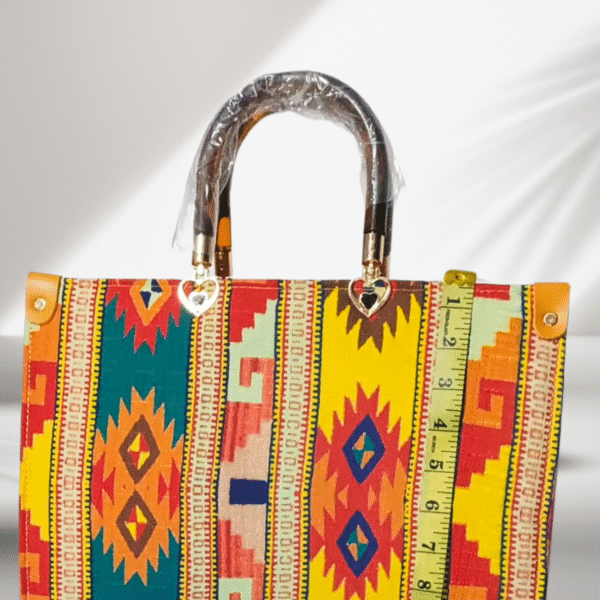 Colorful tribal pattern handbag with yellow tones, acrylic handle, and shoulder strap displayed on a white platform